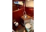 Compact boat head with a small sink and handheld shower, wood-paneled walls, and a marine toilet next to a grated floor.