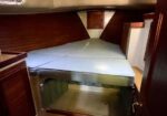 Boat cabin with a V-shaped bed, light blue cushions, and wooden paneling; a hatch/storage area beneath the bed.