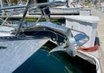 Close-up of a luxury yacht bow with a polished stainless steel anchor mounted at the prow, dock and marina in the background