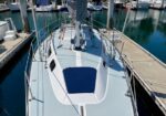 Top-down view of a white sailboat docked at a marina, deck lines and rigging visible, calm blue water nearby.