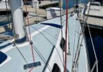View of a sailboat deck in a marina with rigging lines, winches, and a cockpit hatch.