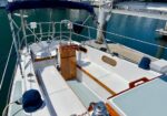 Sailboat cockpit at a marina with white cushions, teak trim, and a central helm pedestal.