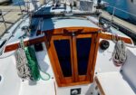 Stern cockpit forward view of a sailboat with a wooden cabin door, coiled ropes on both sides, at a marina