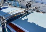 Sailboat deck with metal rigging and track hardware across the cockpit, casting shadows on the light blue surface.
