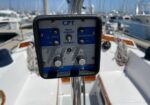 Panel display labeled CPT on a sailboat cockpit, showing hold/heading, port/starboard controls, and dials with a marina background.