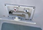Water inlet panel on a boat with red-hot and blue-cold knobs and a spout, set in a white hatch.