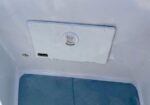 Close-up of a white access panel with a circular latch on a wall, above a blue textured floor mat (likely boat/trailer interior).