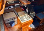 Interior of a boat galley with a small stainless sink, faucet, wooden cabinetry, and a compact stove/oven on the counter