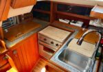 Cozy boat galley with wooden cabinets, a compact oven-stove, cutting boards, and a stainless steel sink.