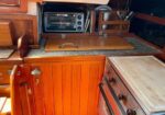 Boat galley with wooden cabinets, a countertop and cutting board, and a toaster oven above the counter.