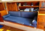 Blue upholstered sofa in a wooden sailboat cabin, with shelves and navigation gear behind.