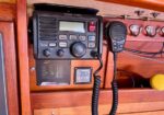 VHF marine radio mounted on a wooden boat panel with a coiled microphone cord and control buttons.