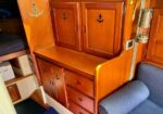 Wooden boat-cabin storage console with doors and drawers, anchor decals, beside a blue upholstered seat.