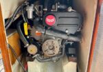 Compact marine engine mounted in a small cabinet with hoses and a belt drive; red emblem on the valve cover is visible.