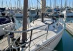 Sailboat docked at a marina with ropes securing it to a pier and other boats in the background