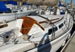 White sailboat docked at a marina with a wooden hatch cover and rigging on the deck