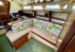 Cozy boat cabin with an L-shaped beige couch and colorful coral-pattern back cushions, wood shelves, and small porthole windows.