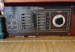 Electrical control panel on a Catalina yacht with labeled AC/DC switches and a large Battery Select dial (All/Off/1/2), wood flooring, and row of circuit breakers for various systems.