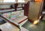 Cozy boat cabin with a coral-pattern upholstered sofa, wood paneling, and a small galley sink on the left.