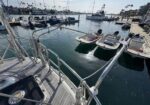 View from a sailboat deck looking toward a marina with moored small boats on a sunny, calm day.