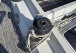 Close-up of a mooring winch on a sailboat deck with white halyard rope coiled around it and wooden deck planks nearby.
