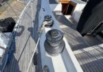 Close-up of two cockpit winches on a sailboat deck with a coiled rope and nearby hatch.