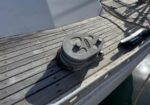 Close-up of a boat deck winch on a weathered wood surface with a coiled rope nearby, casting a shadow.