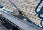 Close-up of a sailboat deck showing a winch and blue lines, with weathered wooden planks and rigging.