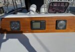 Wooden boat helm panel with two round gauges on sides and a center digital display showing navigation data.