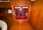 Red electrical control panel with many labeled switches mounted in a wooden cabinet on a boat interior.