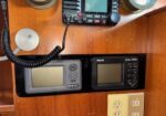Two marine navigation displays mounted in a wooden cabin wall with a handheld mic connected to a radio above them, in a recessed shelf.