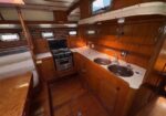Wooden boat galley with double sink, stove, and curved countertop under warm cabin lights.