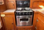 Gas stove with four burners and built‑in oven, stainless steel, mounted in a wooden boat galley with a microwave above.