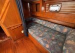 Cozy sailing yacht interior with a built‑in blue patterned sofa along a wood-paneled wall and a small window