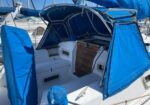 Sailboat cockpit with bright blue canvas covers, white seats, and a wooden hatch door in the center.