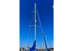 Sailboat in a marina with a tall mast and blue sail cover under a clear blue sky.