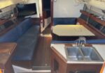 Sailing boat cabin with blue cushioned benches, a wooden table, and a double sink in the foreground.