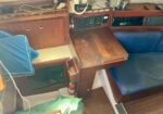 Wood-paneled boat cabin with a built-in desk, navigation electronics, blue seating, and a small red fire extinguisher nearby.