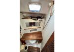 Small boat head with toilet, wooden bench, handheld shower, and a porthole hatch above.
