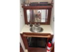 Compact boat galley with stainless sink, cream counter, and a wooden cabinet with a mirror; a fire extinguisher sits to the right.
