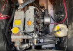 Compact diesel engine in a tight compartment with yellow caps, multiple hoses, and a translucent coolant reservoir on the right side.