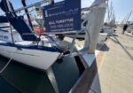 Sailboat docked at a marina with a blue sign advertising Shoreline Yacht Group for Bill Forsythe, 949-466-2206.