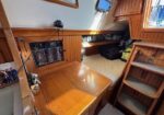 Cozy wooden sailboat cabin with a chart desk, navigation panel, and a bed adjacent to built-in stairs.