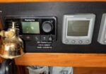 Maritime cockpit panel with a Raymarine marine display and a Tridata instrument mounted on a wooden dash, plus control knobs nearby.