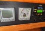 Close-up of a boat's instrument panel: left digital display, middle analog wind gauge, right Cotek remote control panel on a wood panel.