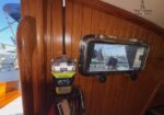 Wood-paneled boat cabin with a rectangular porthole hatch and a yellow/black emergency radio mounted on a rope by the wall.