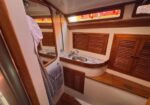 Wood-paneled boat head with sink, marble countertop, mirror, and louvered cabinets; towel hanging nearby.