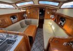 Cozy wooden boat cabin with beige cushioned seating along both sides, a central wooden table, built-in cabinets, and overhead skylights