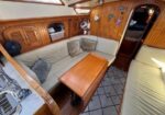 Cozy yacht salon with beige U-shaped seating, wooden table, and wood-paneled walls.