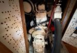 Diesel engine in a tight boat engine room with hoses and wiring surrounding the gear housing.